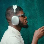 A man wearing stylish headphones and sunglasses in a teal room, capturing modern music vibes.